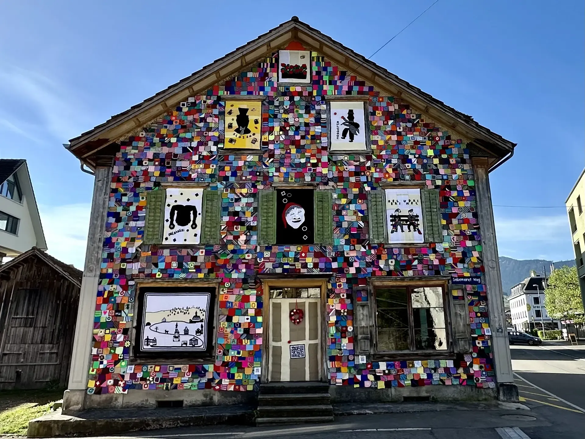 Front side of a historic wooden 3-story Swiss house decorated with thousands of colorful knitted yarn squares.