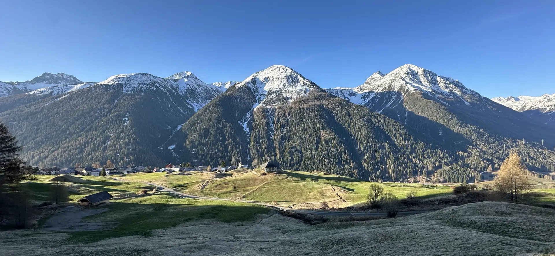 View of the sun terrace that holds the village of Guarda illuminated by the morning sun under a blue sky and against a backdrop of snow-capped mountains.