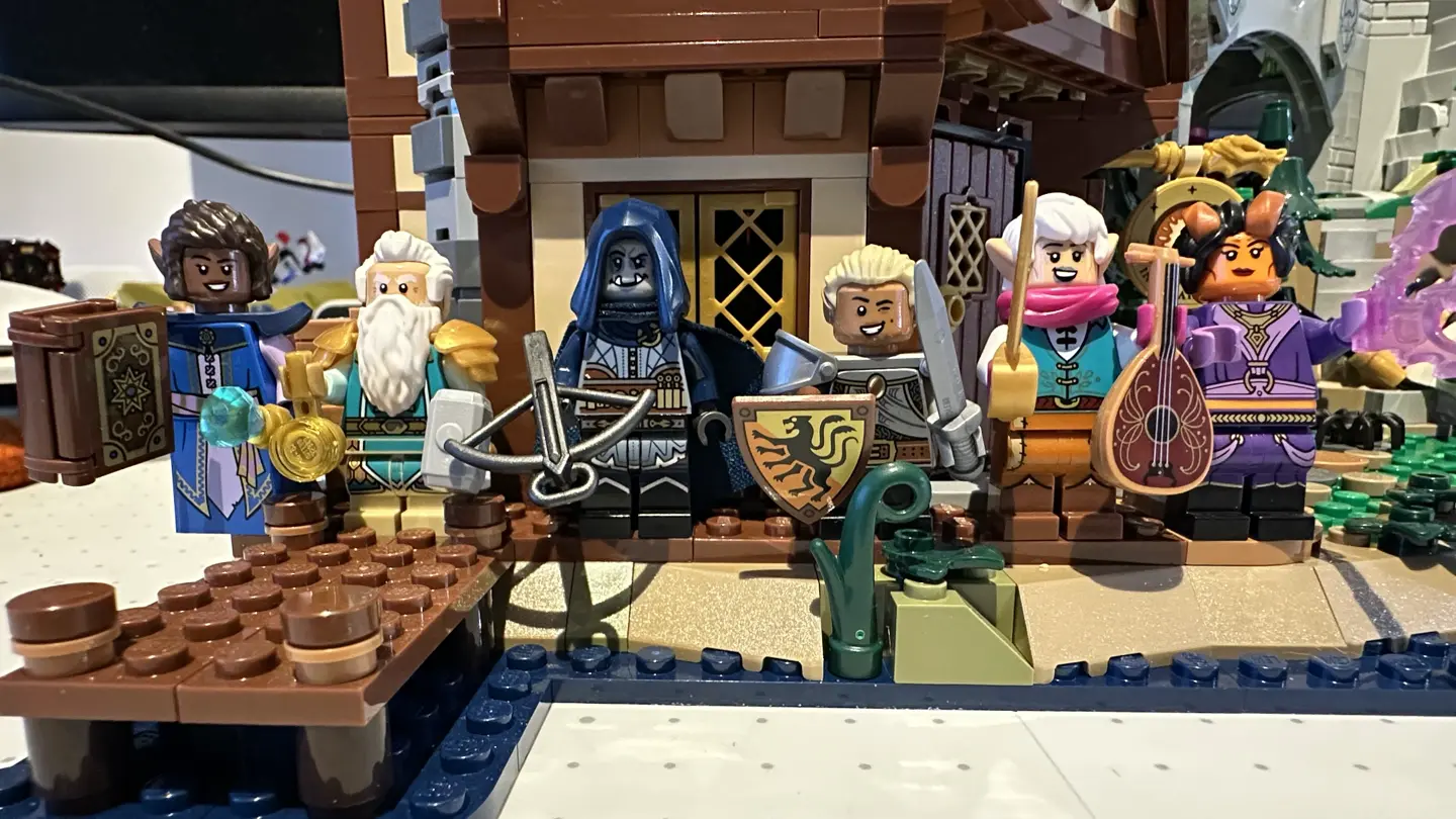 Six LEGO minifig adventurers lined up in front of LEGO set 2138. From left-to-right they are: elf wizard, dwarf cleric, orc rogue, gnome fighter, half-elf bard, and tiefling warlock