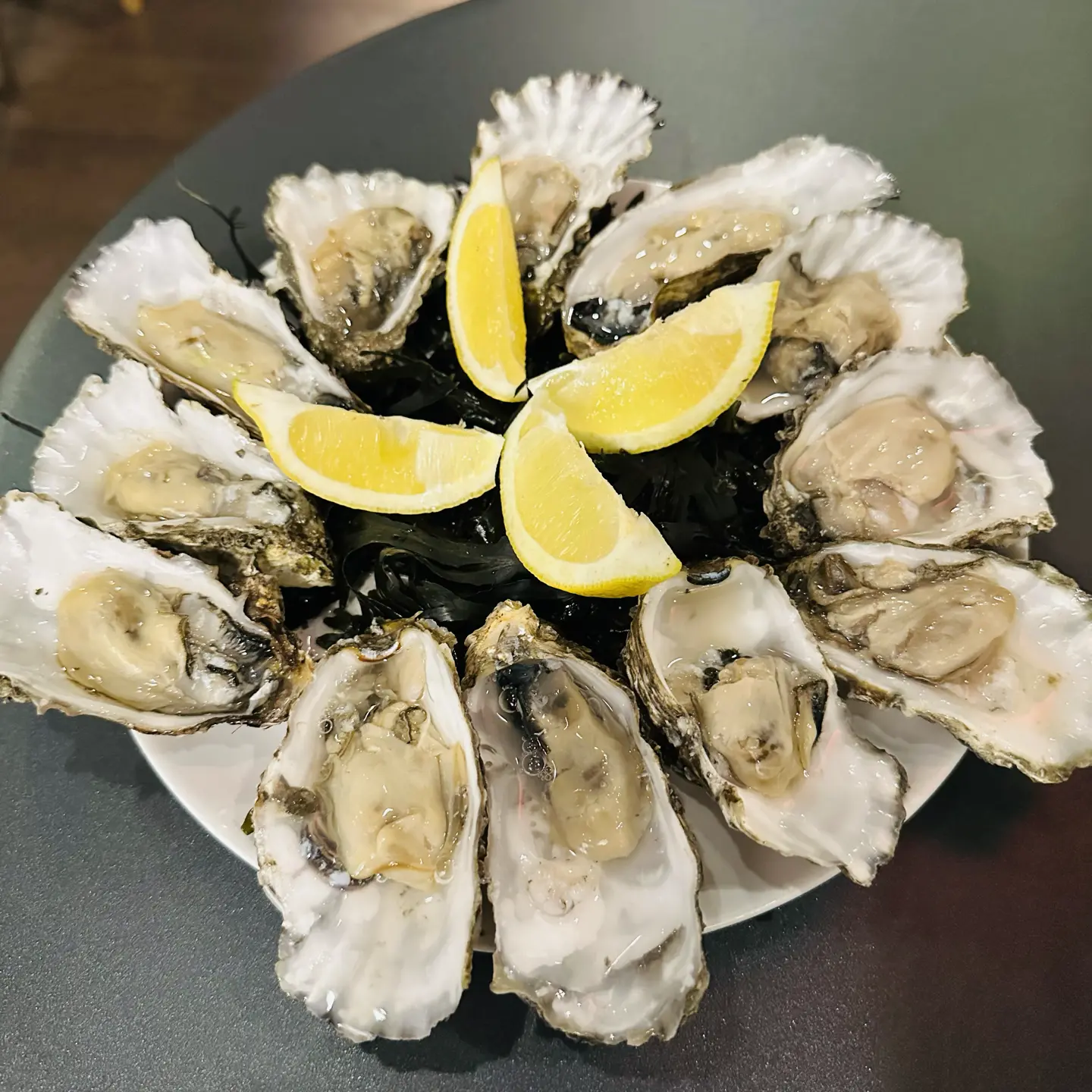 A plate of 12 oysters on the half-shell with 4 lemon wedges