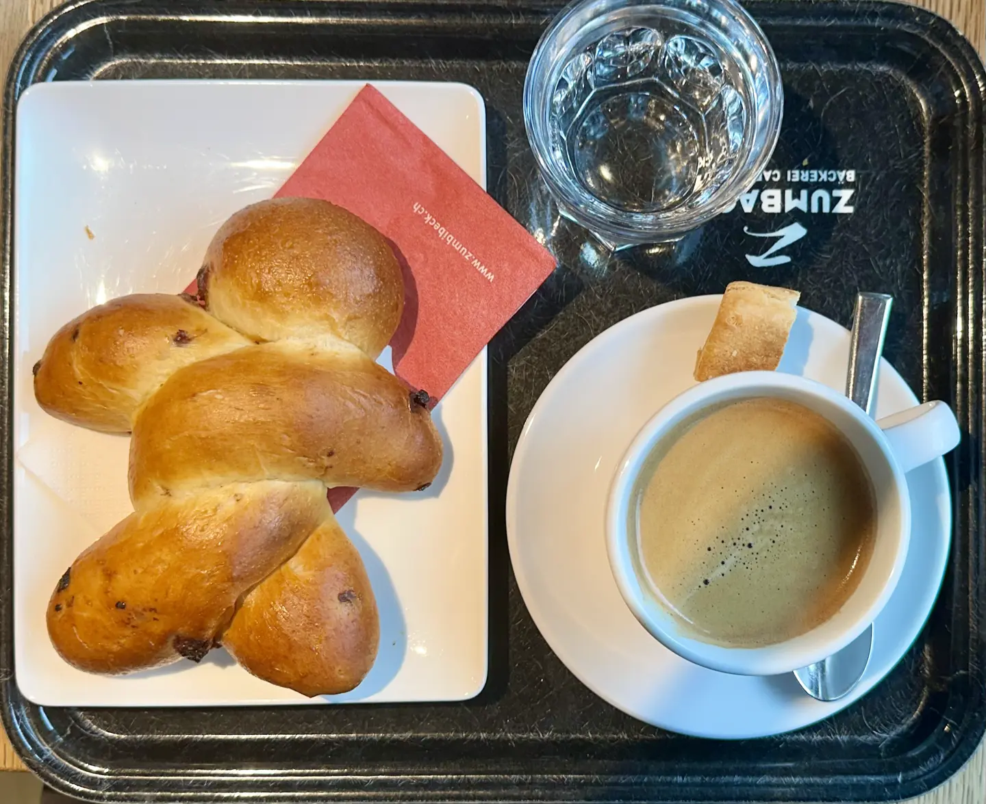 A tray holding a cup of coffee, a glass of water, and a tasty-looking bread man