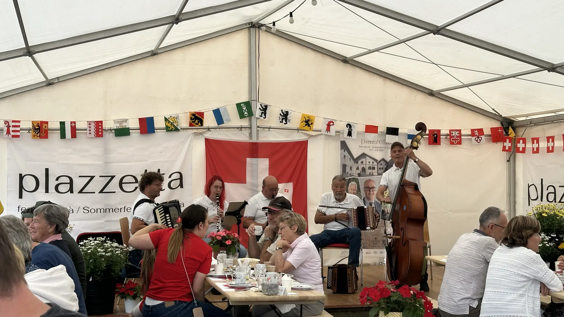 A traditional Swiss music group performs on stage in a tent where people enjoy 1. August brunch under a white tent.