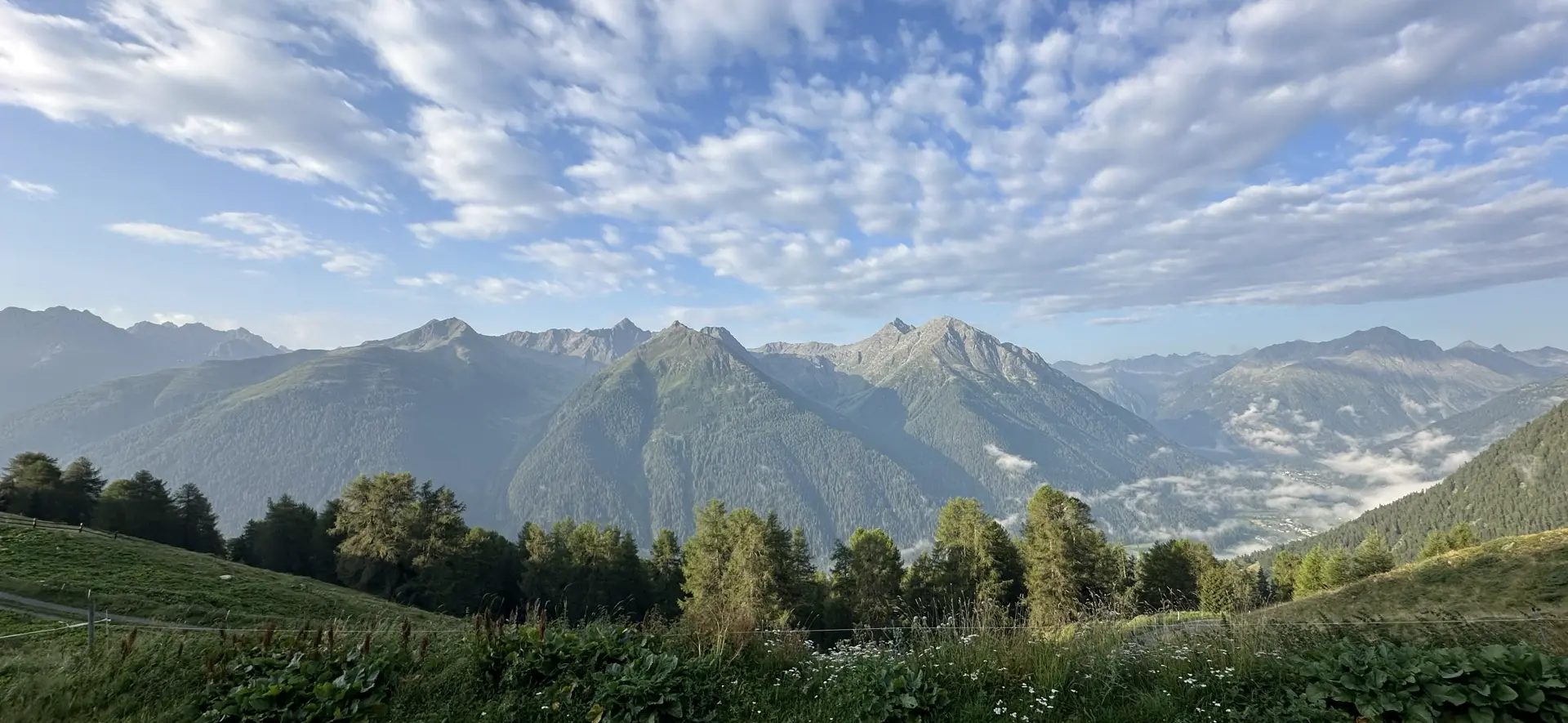 Panorama of the lower Engadine from Alp Sura (2,118m) on a morning with blue sky and puffy white clouds (also some low clouds obscuring Lavin to the right).