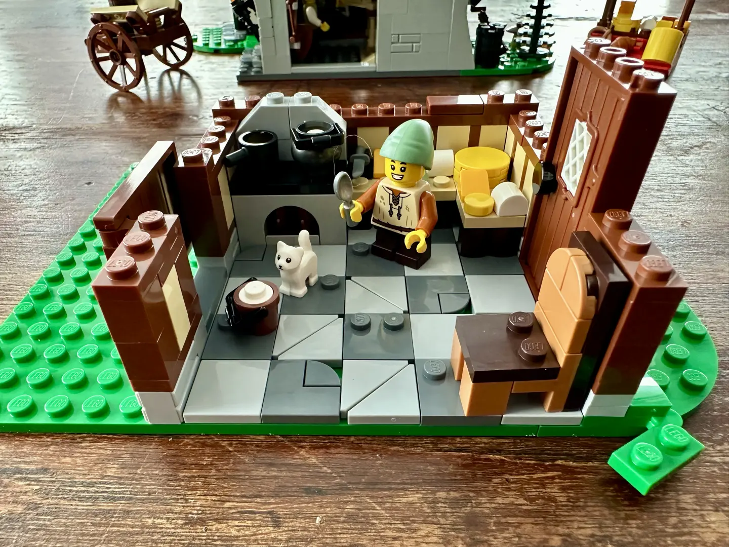 Groundfloor of LEGO cheesemaker's shop with a counter full of different kinds of cheese, a white kitten eyeing a pail of milk, and a small boy holding a spoon.