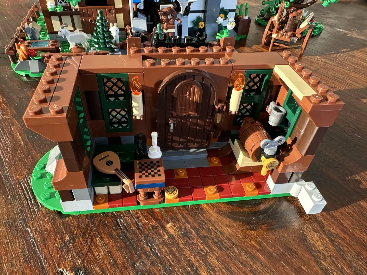 Ground floor of a LEGO tavern. Walls are brown wood inset with dark green latticed windows. There is a tapped keg, a lute, and a board game, but only one place to sit.