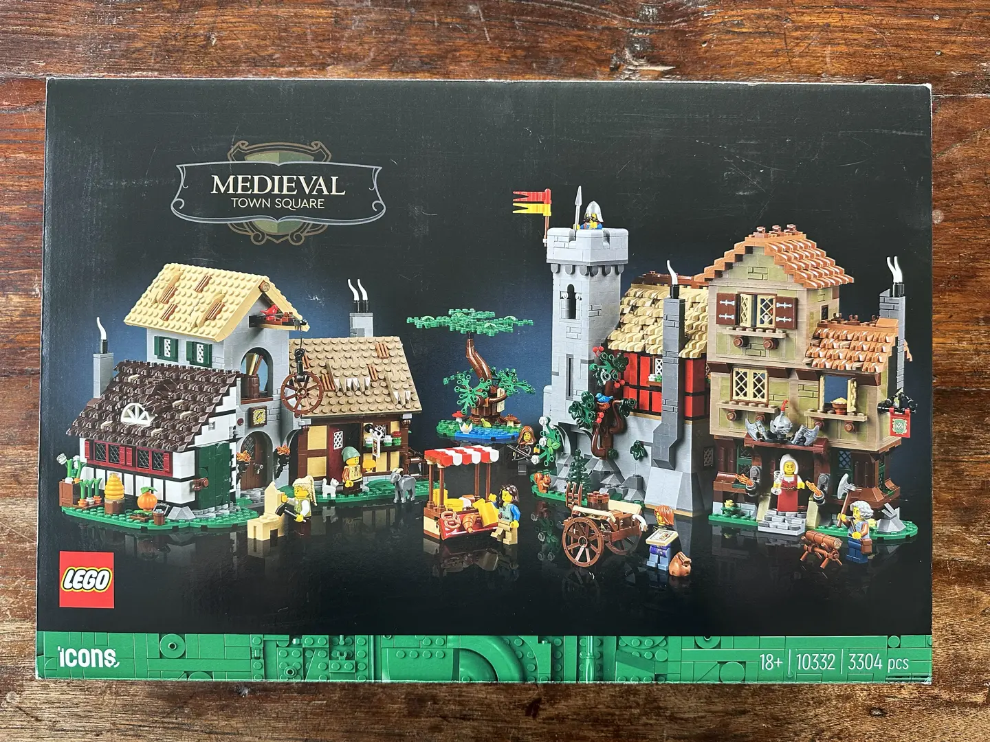 Box front for LEGO set 10332: Medieval Town Square. Box art depicts two clusters of medieval buildings, a tree, and some carts. Various villagers stand around pursuing their respective trades. Set is rated 18+ with 3,304 pieces.