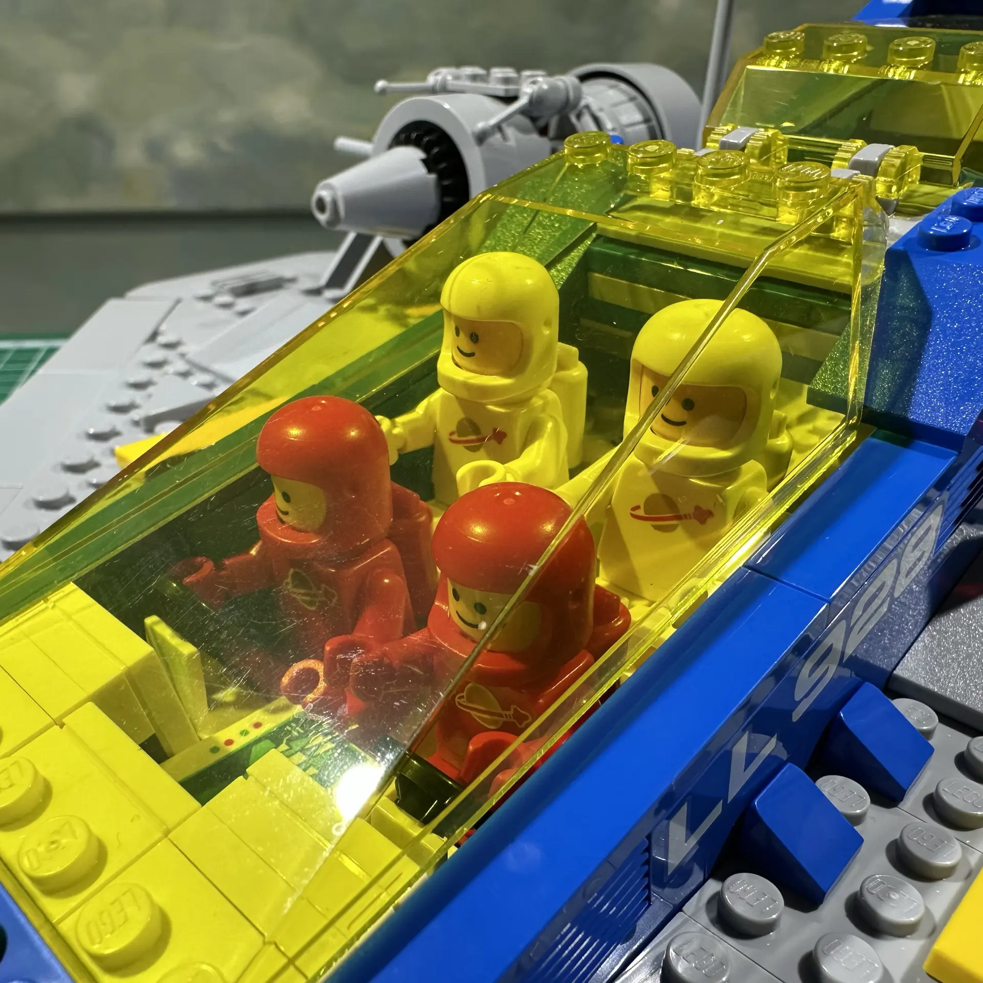 Closeup of the cockpit of LEGO set 10497 showing four astronauts seated under a large transparent yellow canopy