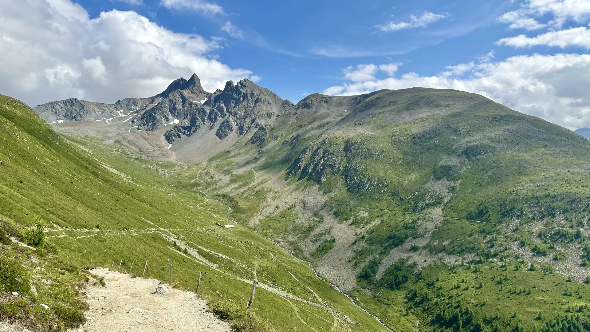 View of high alpine valley clearly left behind by a glacier. The sides are green but the bottom and upper end are dark gray scree.