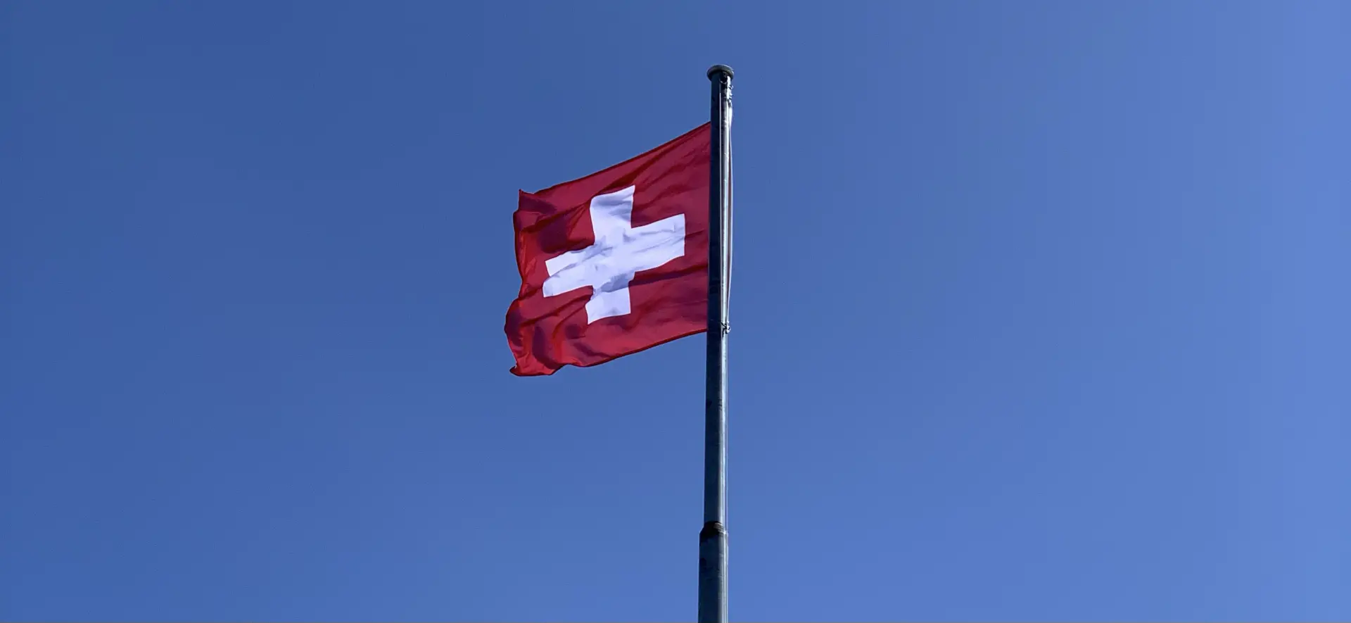 A Swiss flag (white cross on red background) fluttering in a breeze against a blue sky